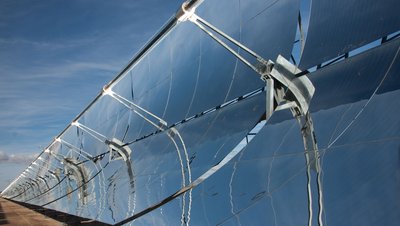 Parabolic trough solar collectors with curved mirrors reflecting blue sky, part of a concentrated solar power plant.