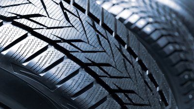 Close-up of a new winter tire tread pattern showing deep grooves, sipes, and zigzag channels for enhanced grip.