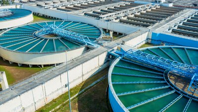 Aerial view of a large water treatment plant with circular tanks and rectangular filtration basins filled with blue-green water.