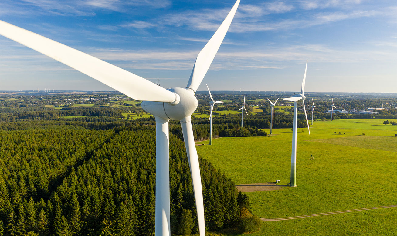 Aerial view of wind turbines in a green landscape – close-up of a rotor in the foreground