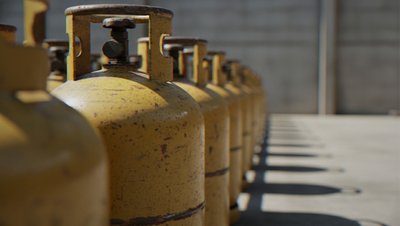 <h3>Propane reflux in an LNG plant</h3> Row of yellow LPG gas cylinders lined up against a concrete wall, casting shadows on the ground.